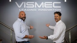 I titolari di Vismec mostrano il logo dell'azienda bianco contro una parete grigia