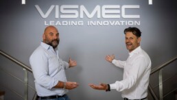 I titolari di Vismec mostrano il logo dell'azienda bianco contro una parete grigia