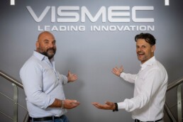 I titolari di Vismec mostrano il logo dell'azienda bianco contro una parete grigia