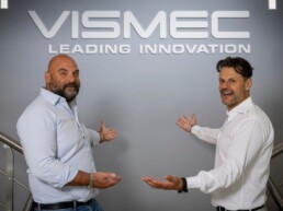 I titolari di Vismec mostrano il logo dell'azienda bianco contro una parete grigia